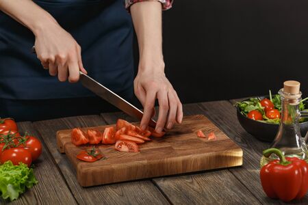Woman cooking fresh salad. Female hands cutting vegetables on board on wooden table.の写真素材