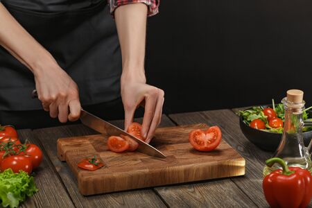 Woman cooking fresh salad. Female hands cutting vegetables on board on wooden table.の写真素材