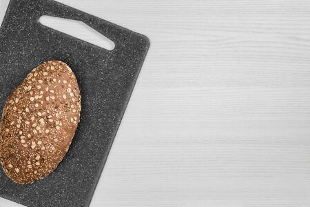 Bread with seeds and flakes on gray cutting board on white