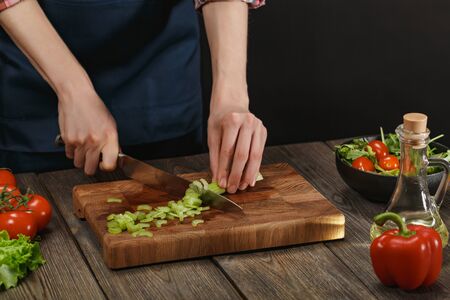 Woman cooking fresh salad. Female hands cutting vegetables on board on wooden table.の写真素材