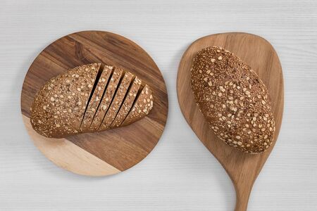Two loaves of bread with seeds and flakes, whole and sliced, on wooden cutting boards on white background top view.の写真素材