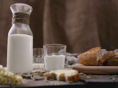 Breakfast in the country with milk and whole wheat bread. Sliced and bitten bread with butter on an old vintage planked wooden table with canvas.の写真素材