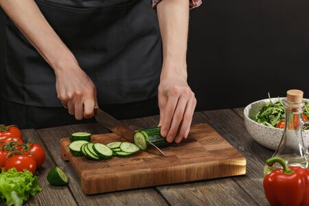 Woman cooking fresh salad. Female hands cutting vegetables on board on wooden table.の写真素材