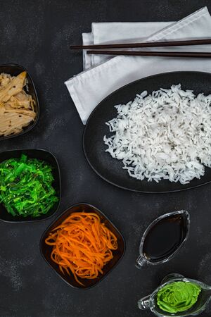 Rice with Korean carrots, soy asparagus, chuka, wasabi, soy sauce and white napkin on blackの写真素材