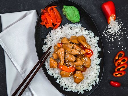 Rice with chicken, pepper, wasabi, ginger, sesame seeds and chopsticks on white napkin on black background. Chinese dish. Horizontal shot.の写真素材