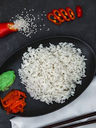 Closeup of rice with pepper, wasabi, ginger and scattered sesame seeds on white napkin on black background. Chinese dish. Vertical shot.の写真素材