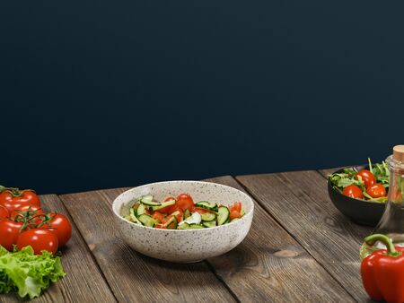 Healthy fresh vegetable salad in a white bowl on a wooden table on a blue background. Horizontal shot.の写真素材