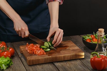 Woman cooking fresh salad. Female hands cutting vegetables on board on wooden table.の写真素材