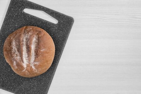 Round loaf of bread on gray cutting board on white background top view.の写真素材