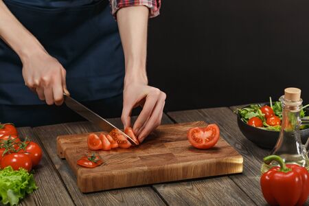 Woman cooking fresh salad. Female hands cutting vegetables on board on wooden table.の写真素材