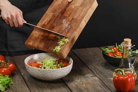 Woman cooking fresh healthy salad. Female hands cutting vegetables on board on wooden table. Diet concept for healthy lifestyle.の写真素材