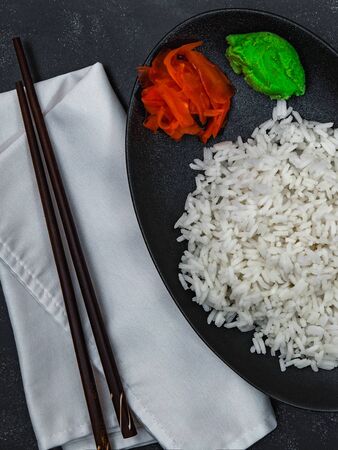 Closeup of rice with wasabi, ginger and chopsticks on white napkin on black background. Chinese dish. Vertical shot.の写真素材