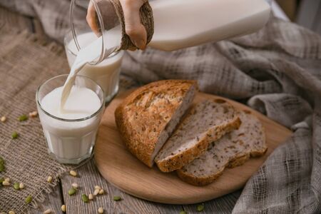 Breakfast in the country with milk and whole wheat bread. Sliced bread on an old vintage planked wooden table with canvas.の写真素材