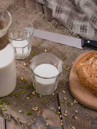 Jug and glasses of milk with scattered seeds and nuts on wooden table with sackcloth.の写真素材
