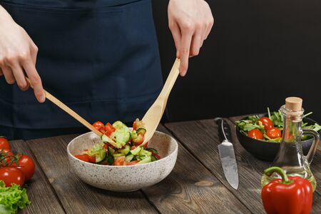 Woman cooking fresh healthy vegetable salad on wooden tableの写真素材