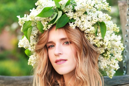 Portrait of young woman in lilac wreath. Girl with lilac flowers on head looking at camera smilingの写真素材