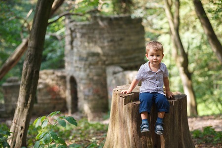 Little boy sitting on a stump. Ruins of the old castleの写真素材