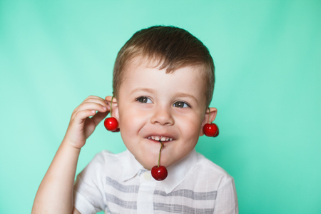Cute boy boy eating ripe cherries, making funny faces and playing with the cherries, having fun.の写真素材