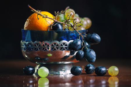 A bunch of grapes in a vintage vase on black background. Autumn still life. Grapes in silver bowl. Closeup.の写真素材