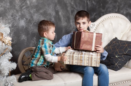 Two brothers sitting on the bed opening New Year's gifts in boxes. New Year's holidays. Christmas