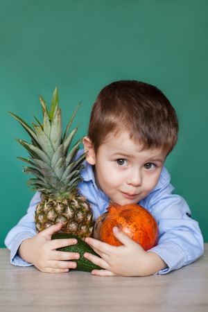Cute little boy with exotic fruits on green background. Concept healthy eating.の写真素材