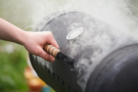 A man's hand opens a metal brazier. Bbq grill with smoke coming out of grillの写真素材