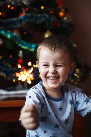 Beautiful Little child holding burning sparkler on New Years Eve, bengal fire. There is a background with multi colored lights.の写真素材