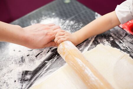 The process of preparation, rolling dough. Children's hands and the dough. In the hands of a wooden...