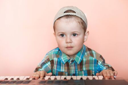 Portrait of a pretty boy wearing baseball cap backwards playing the digital piano.