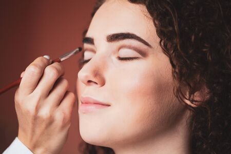 Beauty and makeup concept - closeup portrait of beautiful woman getting professional make-up with brush.の写真素材