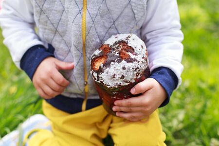 Happy little boy eats Easter Cake, in spring garden, outside. Cute happy little boy at spring green grass and blooming garden, eating Easter Cake and having fun outdoors.の写真素材