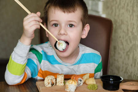 Child Eat Sushi Rolls At Home. Happy boy ready for eating sushi.の写真素材