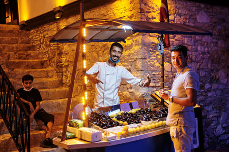 Kusadasi, Turkey - 07.22.2021: Man selling raw mussels in shells served with lemon juice. Streets of Kusadasi. Kusadasi night life. Turkey vacationのeditorial素材