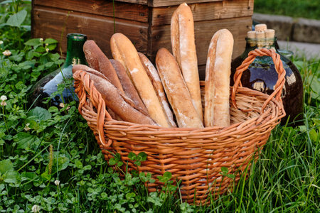 Wicker basket full Of Baguettes on green grass in park, near large bottles with wine.の写真素材