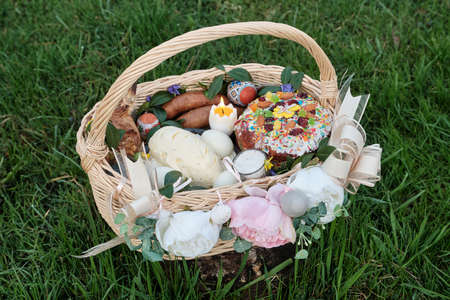 Ukrainian Easter basket filled with traditional festive dishes. Easter food, easter eggs, cheese, butter, ham, Easter bread and basket. Basket on a green grass meadow.の写真素材