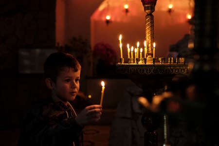 Little boy holding candle on dark background. A Child lights a candle in a chapelの写真素材