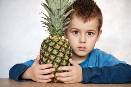 Cute Caucasian 7 year old boy with brown eyes holding a pineapple looking at the camera. Close up portrait image.の写真素材