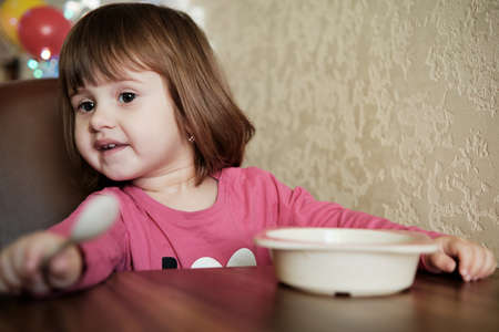 Happy Little Girl Eats With A Spoon While Sitting At Table. The Concept Of Healthy Eating.の写真素材