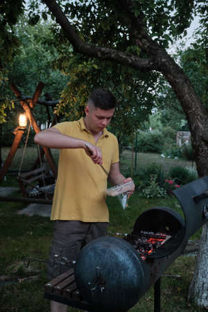 Handsome Male Preparing Barbecue Outdoors. Fresh sausage and hot dogs grillingの写真素材