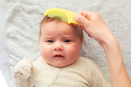 Mom combs a newborn baby with a special hair brush. Maternity concept. Baby hygieneの写真素材
