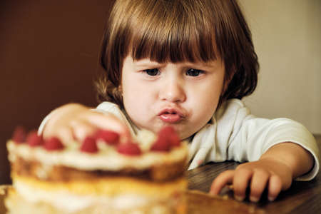 Cute Happy Baby Girl Eating Cake With Raspberries. Adorable little girl Tasting Cream On Cake. close...