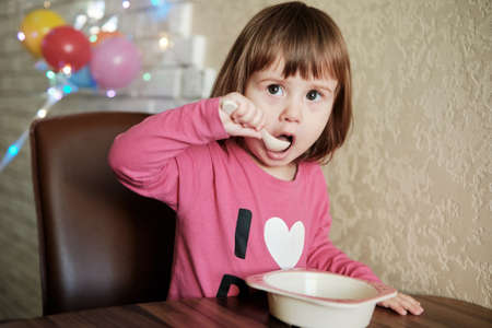 Cute Little Girl 2 Years alone eats porridge with a spoon. Child eat concept.の写真素材