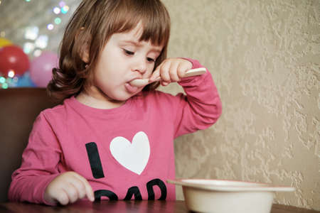 Cute Little Girl 2 Years alone eats porridge with a spoon. Child eat concept. Child eat concept.
