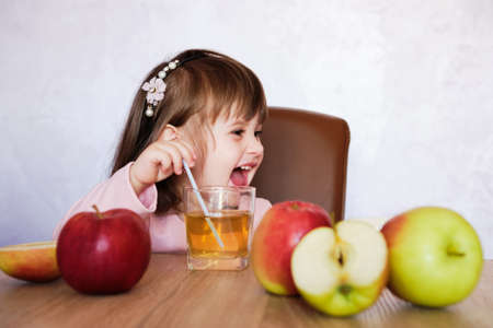 Happy little girl with glass of juice. Baby girl with juice and fruit apples. Healthy food.の写真素材