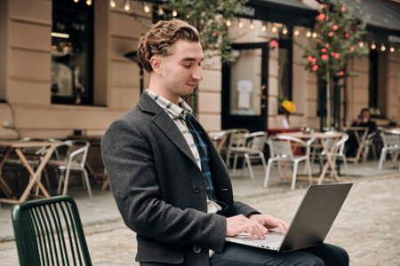 Attractive young bussiness man working on laptop computer while sitting outdoors. Freelance young guy work with computer outside.の写真素材