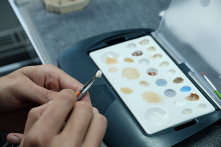 Dental technician coloring dental prosthesis with a paint brush at the laboratory. Aesthetic coloring of teeth. Concept of implants producing.の写真素材