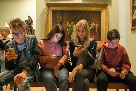 Lviv, Ukraine - September 16, 2018: A group of noisy schoolchildren with phones in their hands are sitting in the Art Gallery. School boys and girls on excursion in museum.のeditorial素材