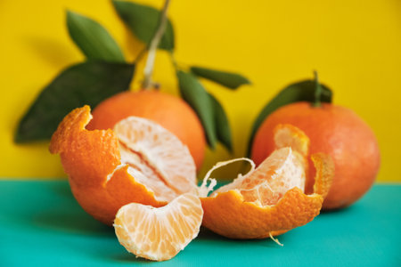 Tangerine or clementine with green leaf and slices on a yellow background