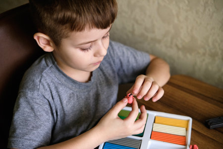 Elementary school age Caucasian child boy plays with plasticine on table, modeling clay, molds,...