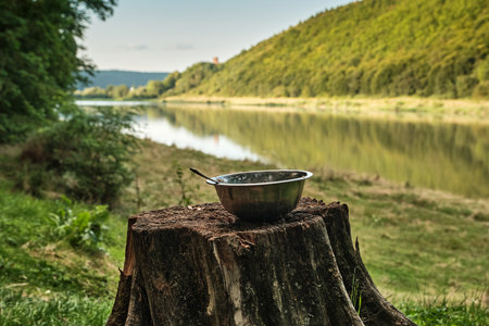 Breakfast by the river. An old stump on the riverbank with a metal bowl with a spoon. A beautiful landscape with a riverの写真素材